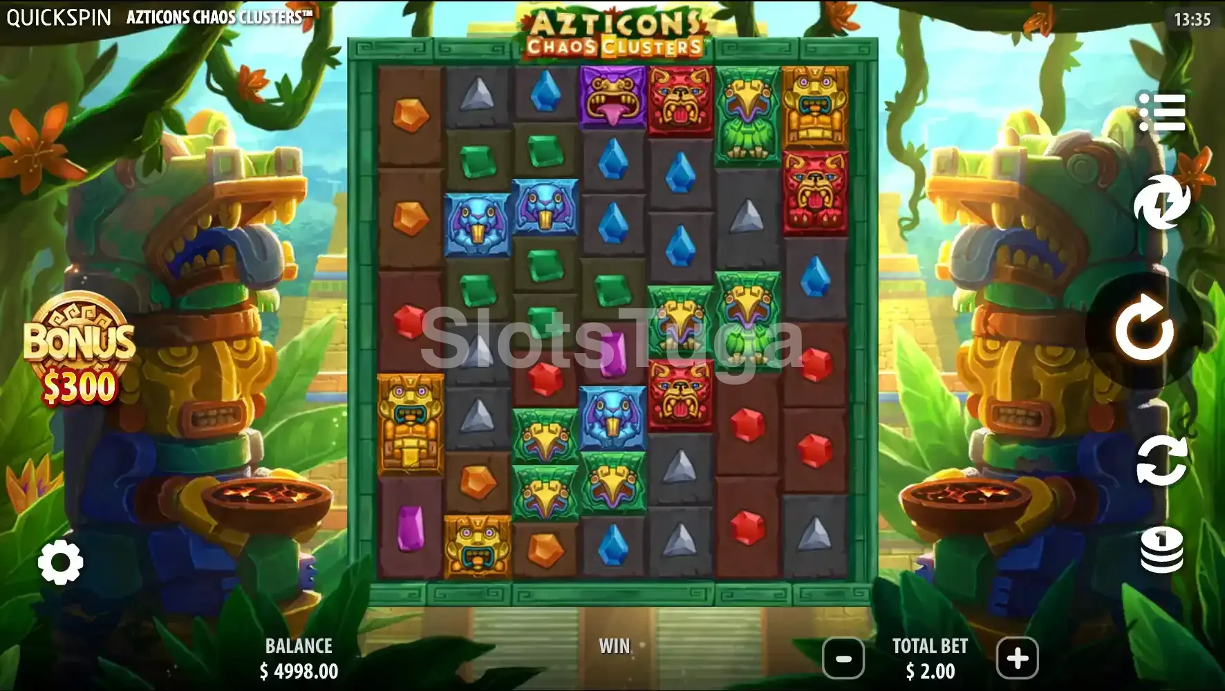 Azticons Chaos Clusters em jogo base: grelha alta em pedra verde com gemas vermelhas, azuis, verdes e roxas, triângulos cinzentos e ídolos coloridos em forma de pássaro e de jaguar, um totem de pedra com uma taça de oferendas de cada lado e o botão de compra do bónus à esquerda, diante de uma pirâmide na selva.
